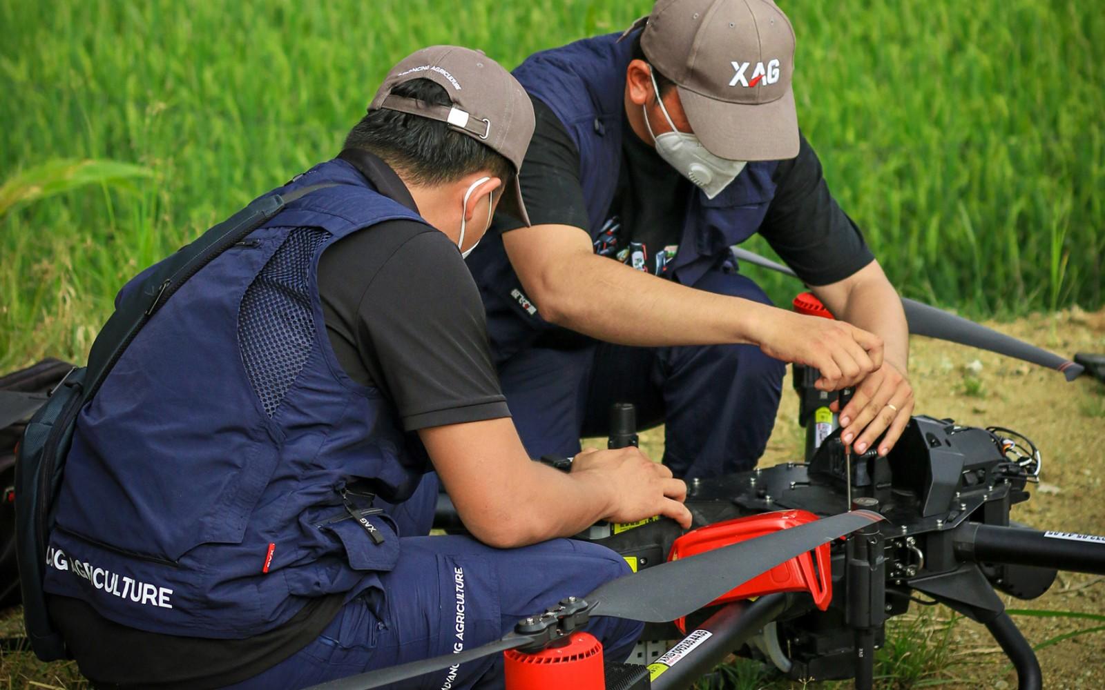 on a bright sunny day, two young drone mechanical engineers are preparing the drone by a rice paddy for its spraying trial. (vietnam, source: vietnam smart agriculture technology joint stock company)